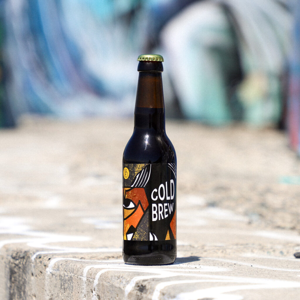 Photo of cold brew coffee bottle on pavement with graffiti in the background